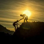 Image of two people helping each other climb a rock