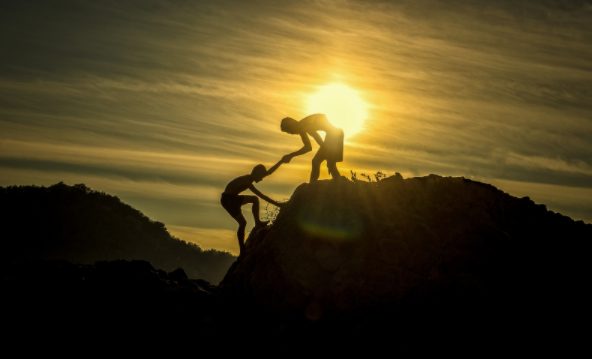 Image of two people helping each other climb a rock