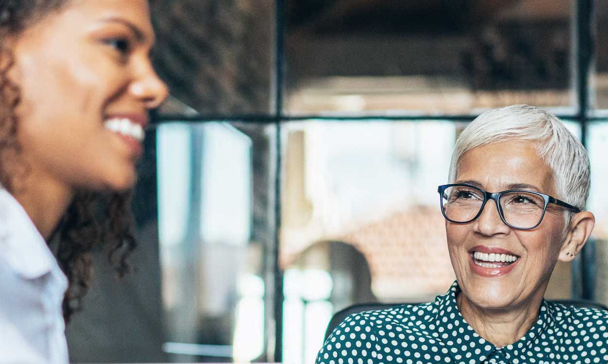 Foundation List Nonprofit Job Postings Site Image of nonprofit meeting between two workers. A women is seen smiling to anther sitting at the meeting table