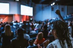 Image of people seated at a nonprofit conference with one women with her hand raised in the air in support and excited.