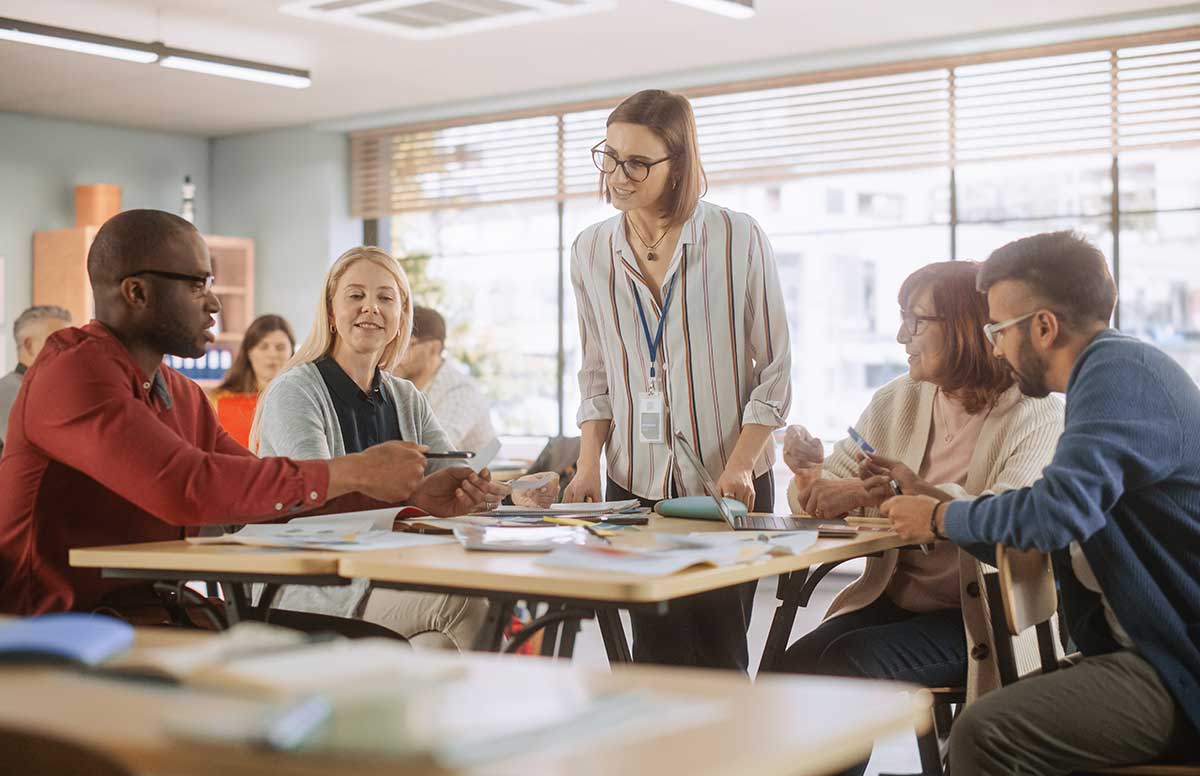 A female adult education teacher stands over her class's work representing that she used foundation list to find education jobs