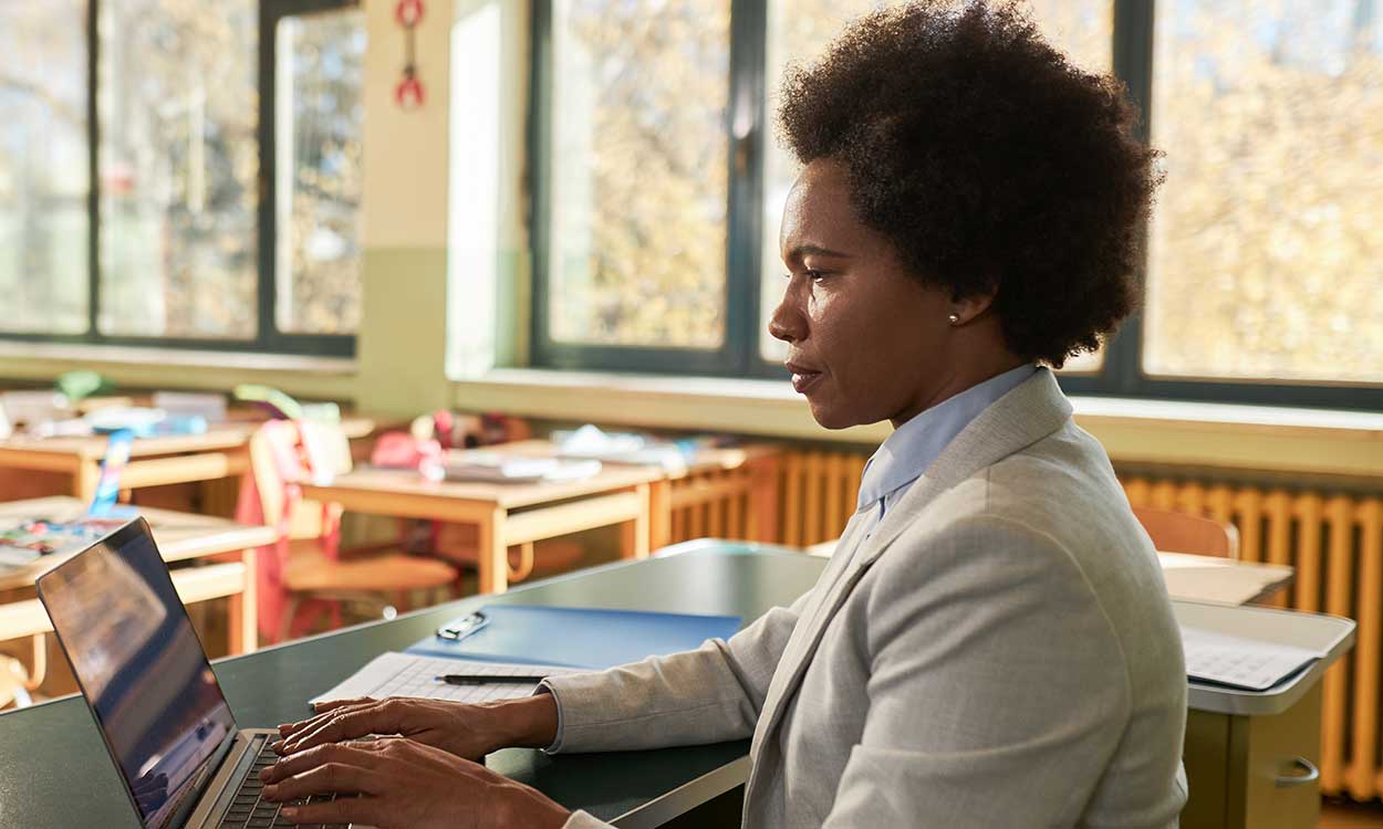 A teacher is seen using a laptop