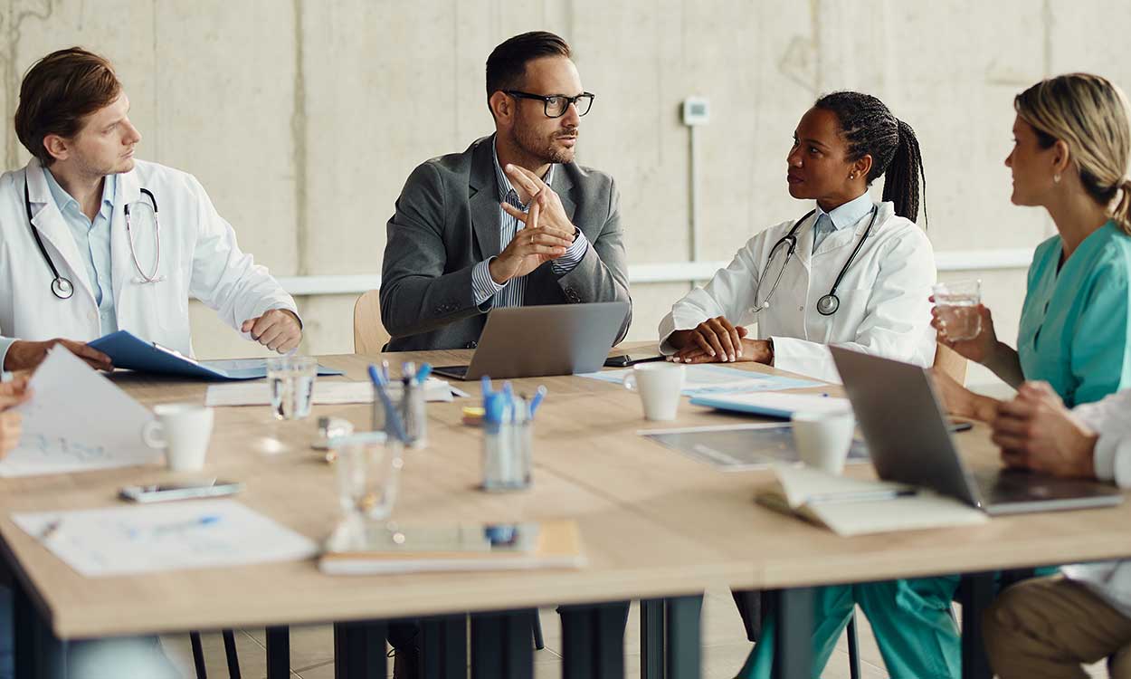 A group of medical professionals sits at a table discussing who to hire to add to their healthcare team