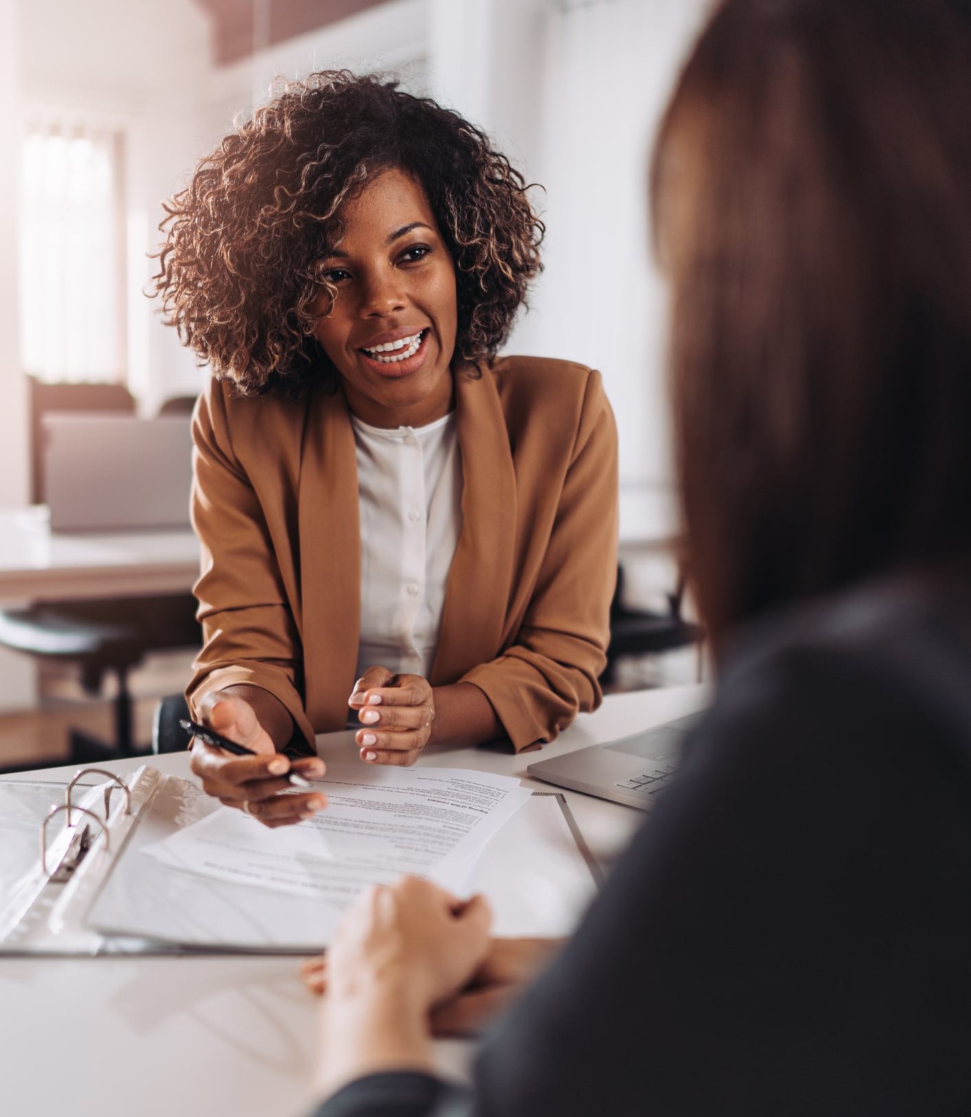 Nonprofit Job Board Recruiters is seen in an interviews she is wearing a brown suit jacket and smiling at the candidate holding a pen
