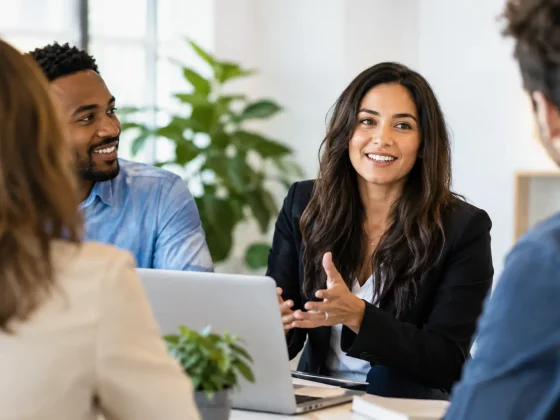 A woman in a dark blazer talking with colleagues around a table