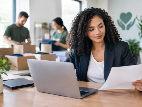 A woman reviewing a document beside an open laptop